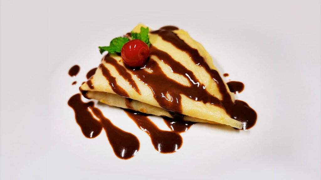 Chocolate drizzled crepe topped with a cherry and mint leaf at Drake Bay Greenleaf.