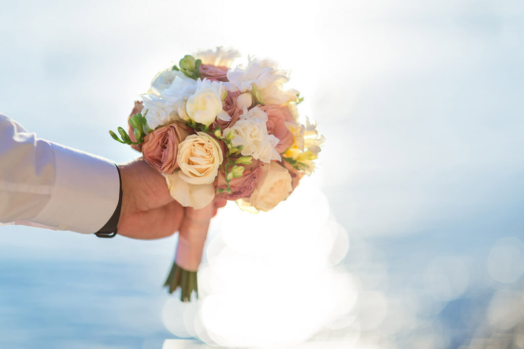 Hand holding a bouquet of white and pale pink roses in soft natural sunlight.