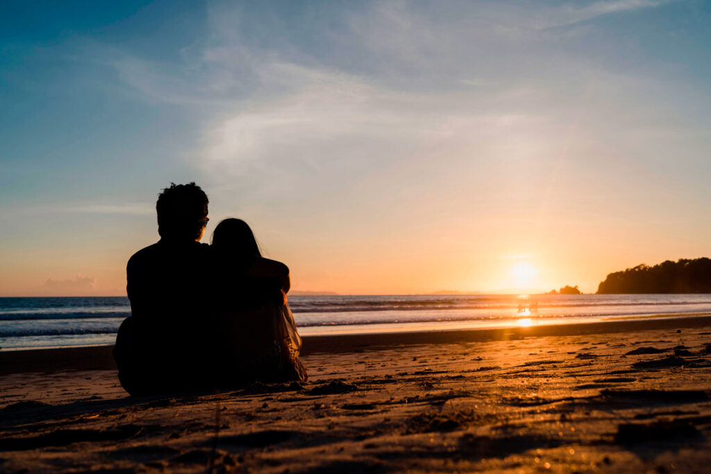 Couple sitting on the beach watching the ocean during a golden sunset in Drake Bay.